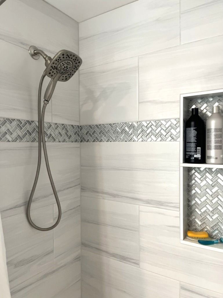 Shower with white marble-look tiles, silver fixtures, a mosaic accent, and a built-in shelf with toiletries.