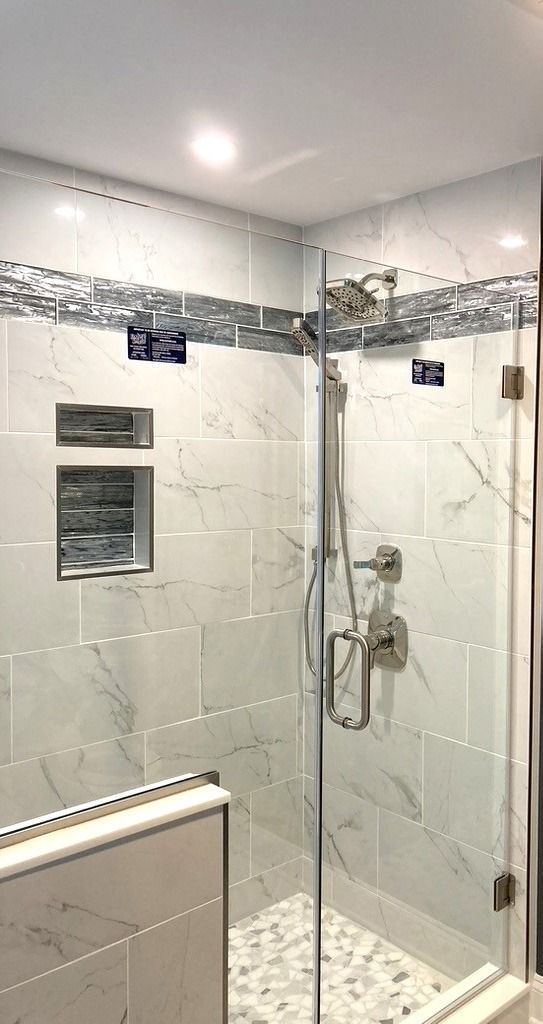 White marble shower with glass door, nickel fixtures, and pebble floor. Decorative tile border.