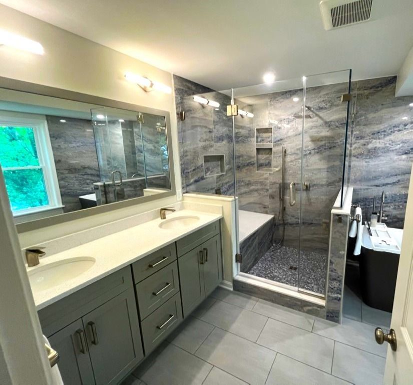Modern bathroom remodel with gray cabinets, marble-look shower, and a glass shower door.