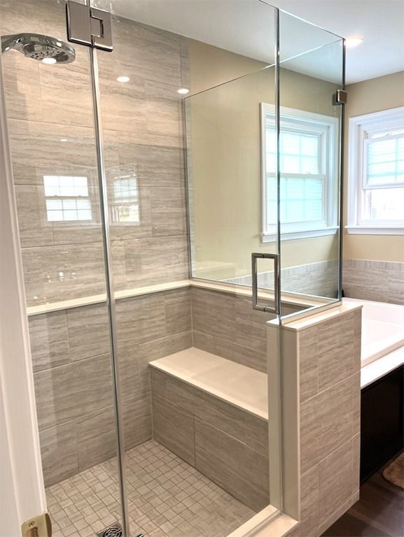Modern shower with glass door, built-in bench, and gray-tiled walls.