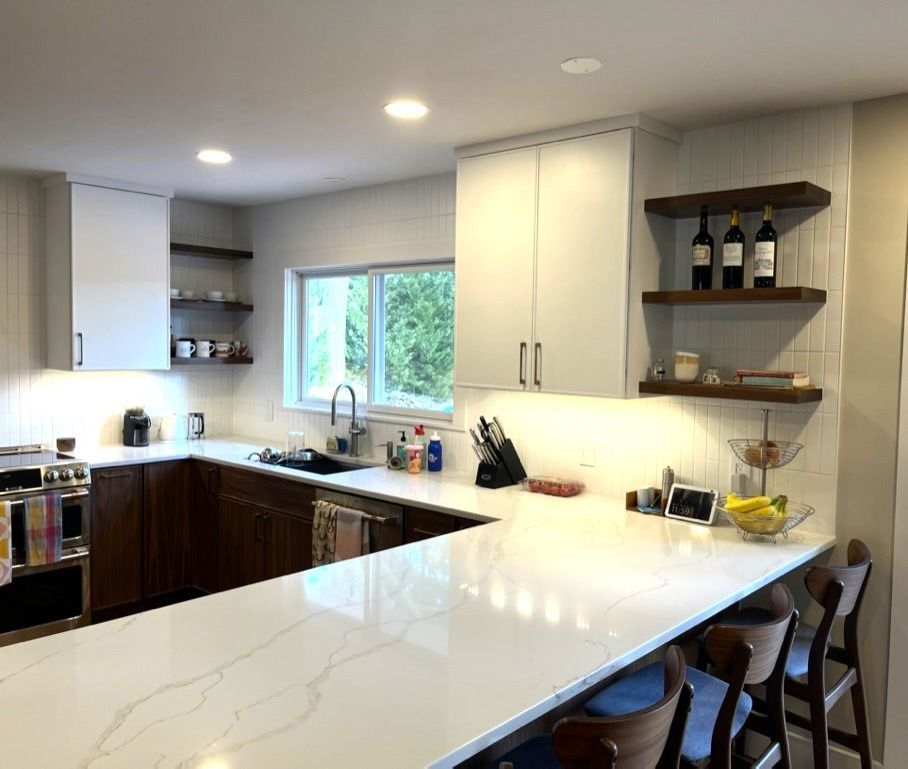 Modern kitchen with white countertops, dark wood cabinets, and shelves with wine bottles.