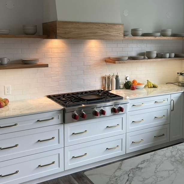 White kitchen with gas range, floating shelves, and white cabinets.