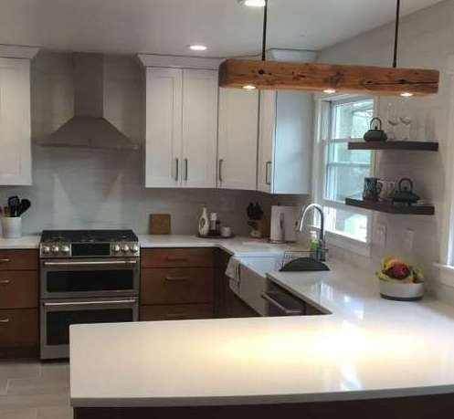 Modern kitchen with white countertops, wooden beam light fixture, and two-tone cabinets.