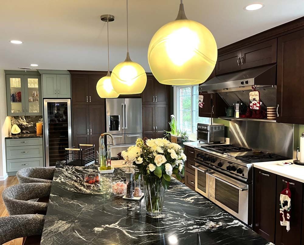 Kitchen with island, dark cabinets, three pendant lights, and stainless steel appliances.