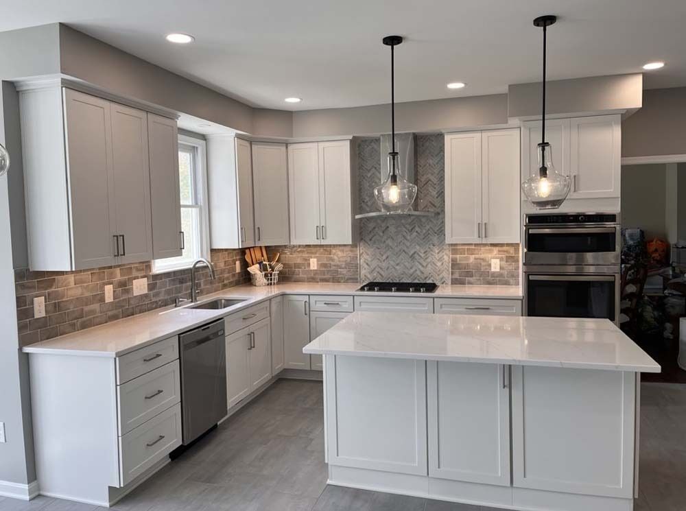 Modern white kitchen with island, stone backsplash, stainless steel appliances, and gray walls.