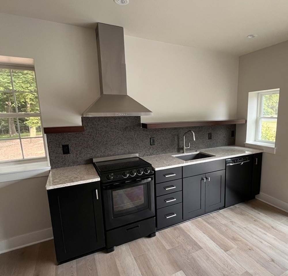 Black and white kitchen with stainless steel range hood, black cabinets, and countertops.