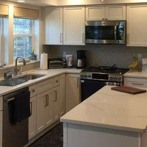 L-shaped kitchen with white cabinets, stainless steel appliances, and a countertop island.