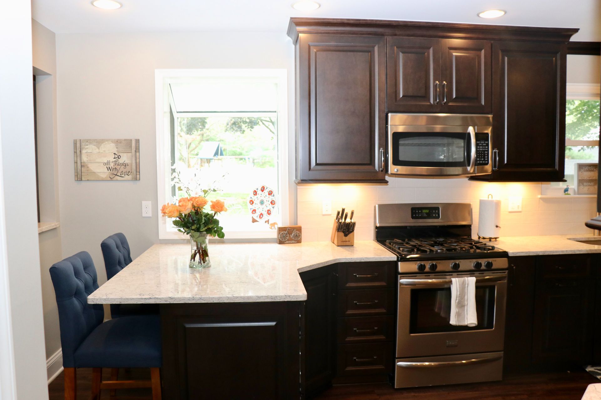 Dark-cabinet kitchen with stainless steel appliances, breakfast bar, and blue chairs.