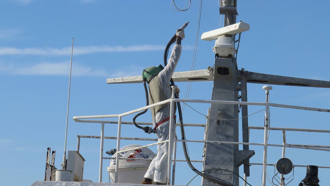 A man is standing on the deck of a boat holding a hose.