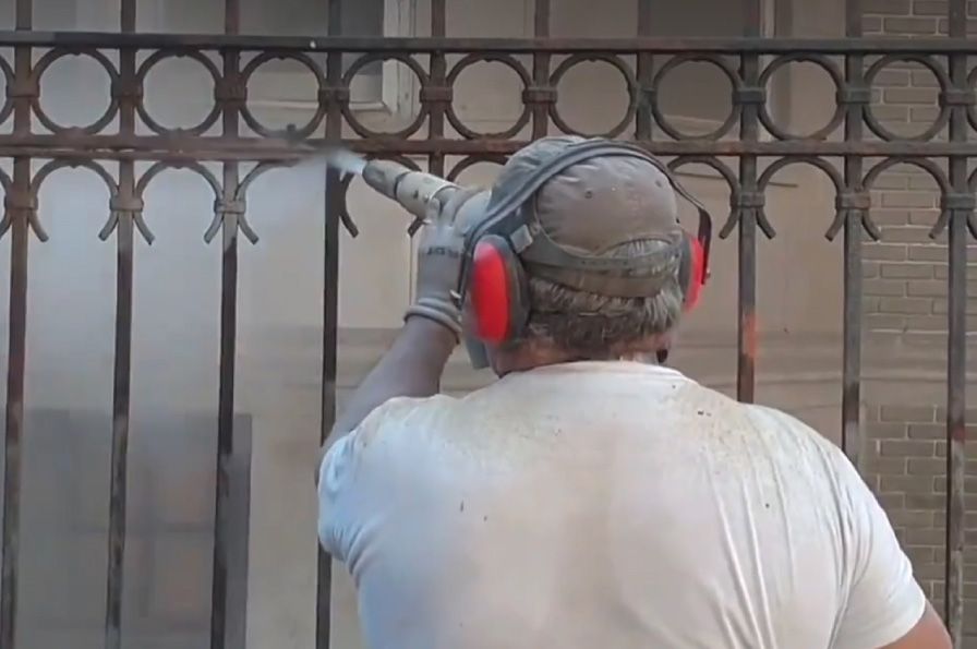 A man wearing ear muffs and headphones is spraying a fence.