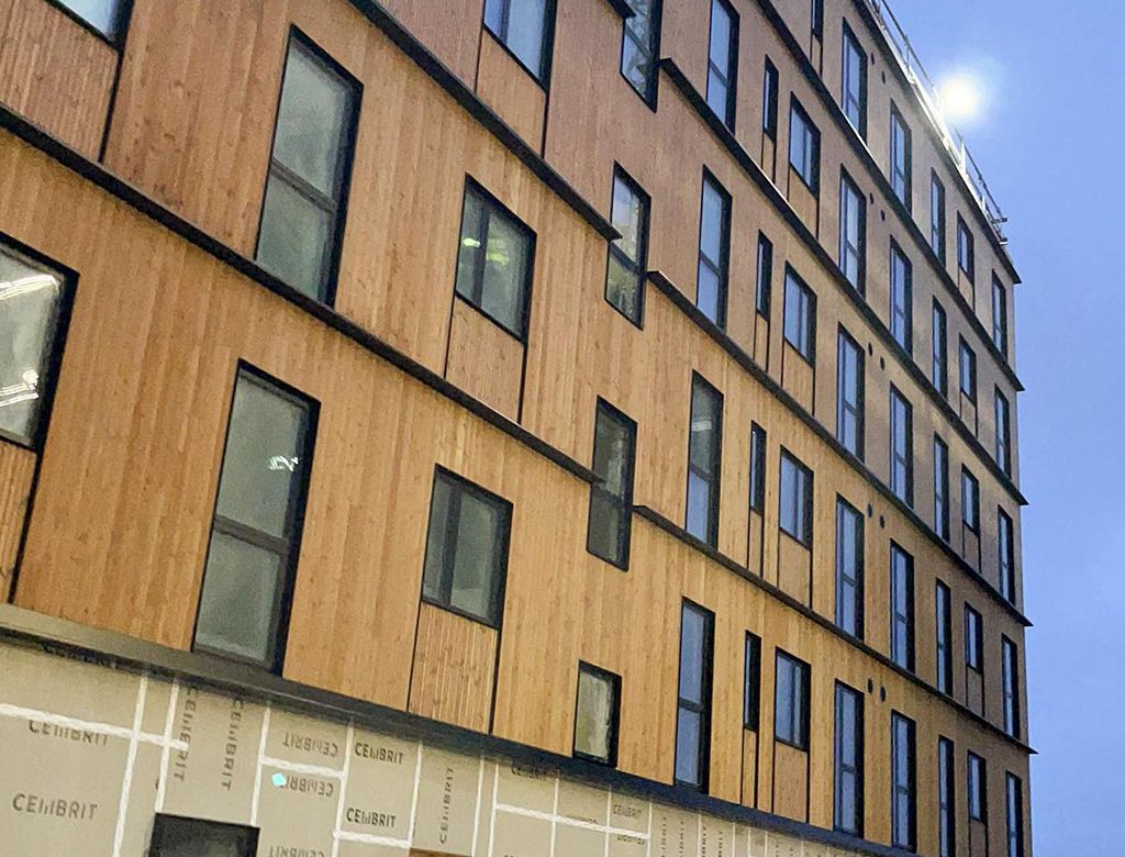 Moderne træbeklædt bygning med mange vinduer, set fra en lav vinkel mod en overskyet himmel.