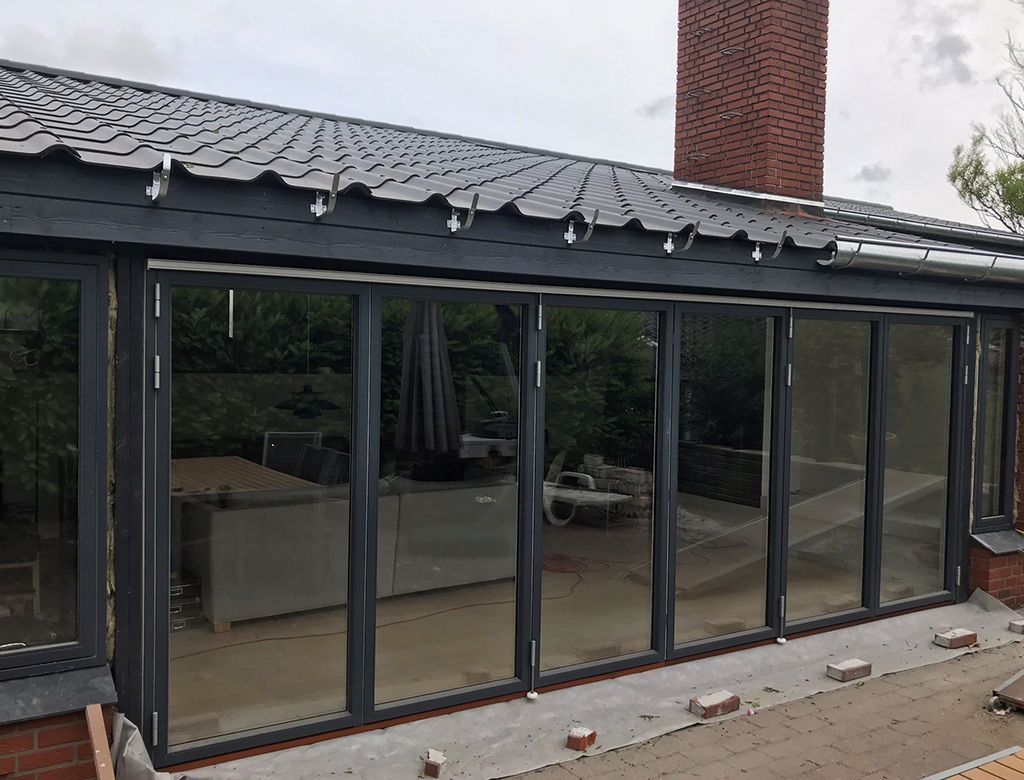 Glasfoldedøre på en tilbygning under et gråt tag og en murstensskorsten.