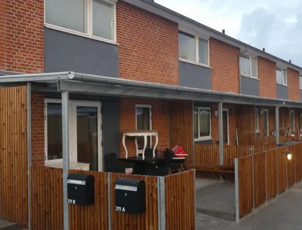 Rækkehuse med overdækkede terrasser. Facade af røde mursten, træhegn, postkasser.