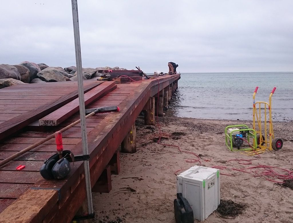 Dokbyggeplads med arbejdere, værktøj og en generator på en sandstrand nær havet.