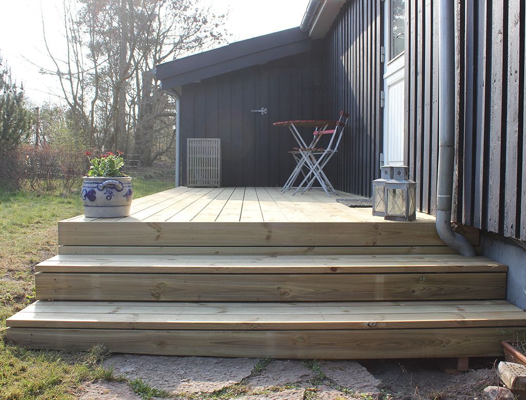 Trætrappe, der fører til en mørk husindgang; en potteplante og et bord er på verandaen.