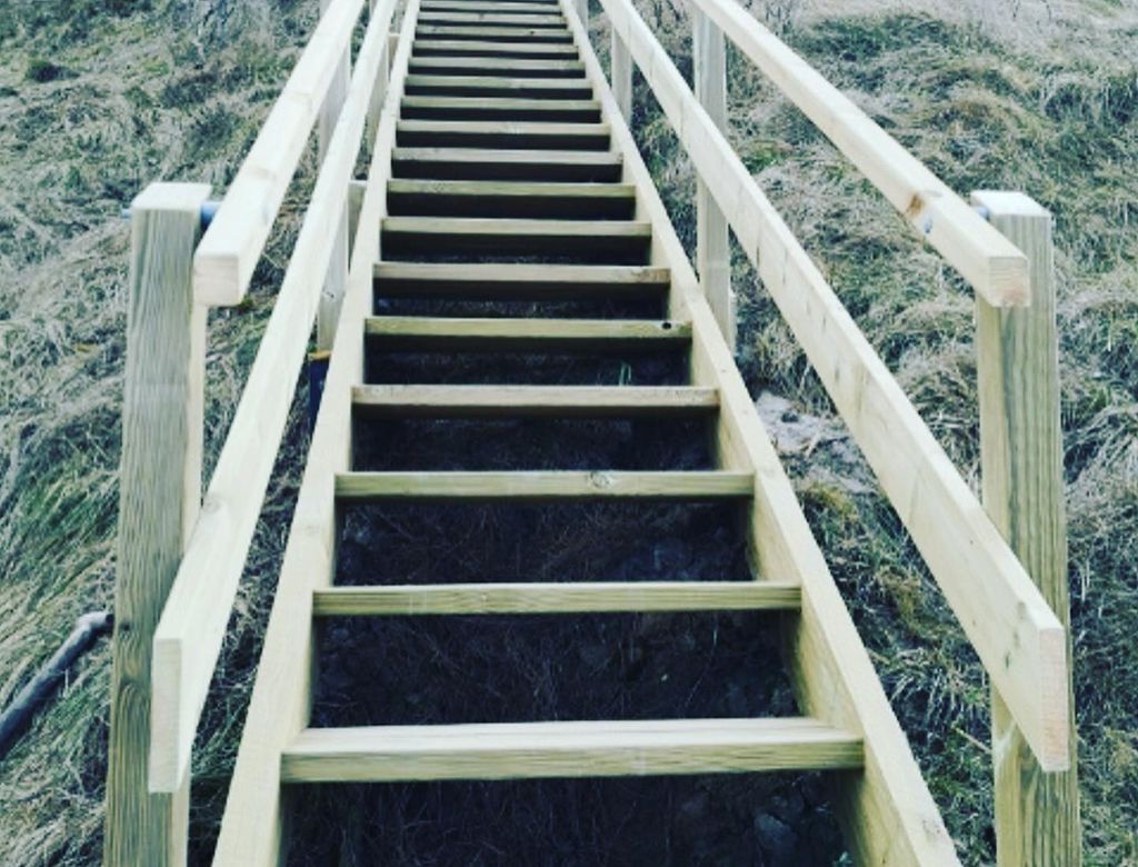 Trætrappe op ad en græsklædt bjergskråning med gelændere på begge sider.