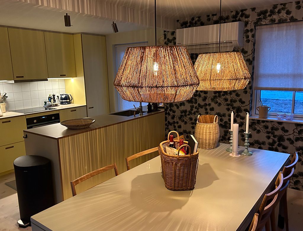 Køkken med gule skabe, køkkenø, spisebord og to pendellamper.