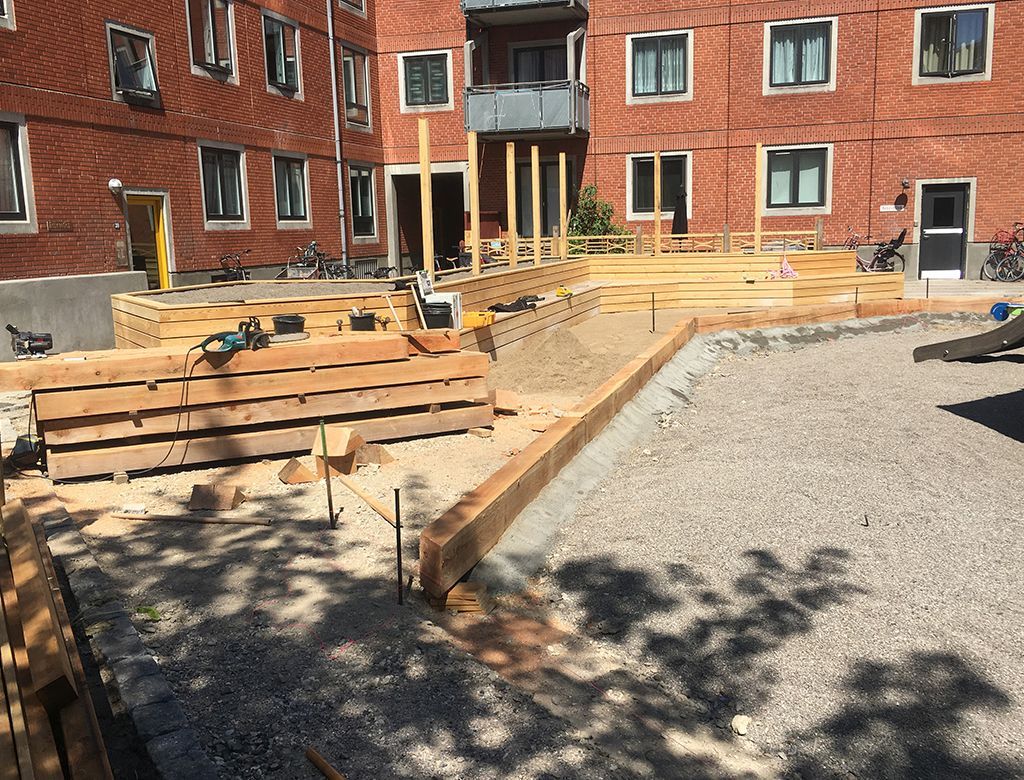 Byggeplads med trækonstruktioner, der bygges på en grusbelægning, foran en bygning af røde mursten.