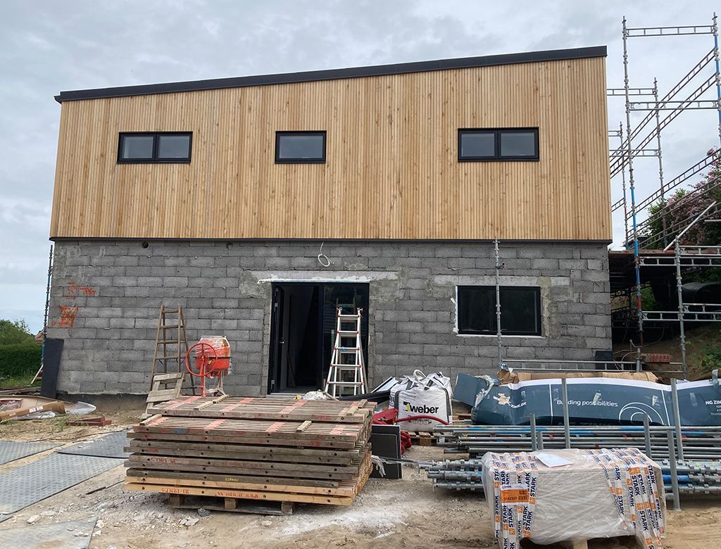 Opførelse af en toetagers bygning med en øvre etage med træpaneler og en nedre etage med grå mursten.