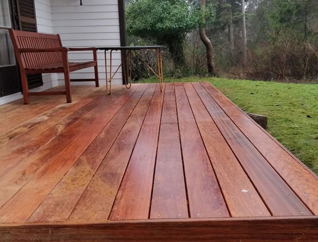 Træterrasse med bænk, rækværk og grøn græsplæne i skovklædte udendørs omgivelser.