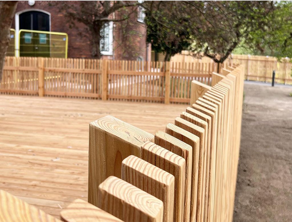 Træterrasse og hegn, nærbillede af hegnets hakdesign med en bygning i baggrunden.