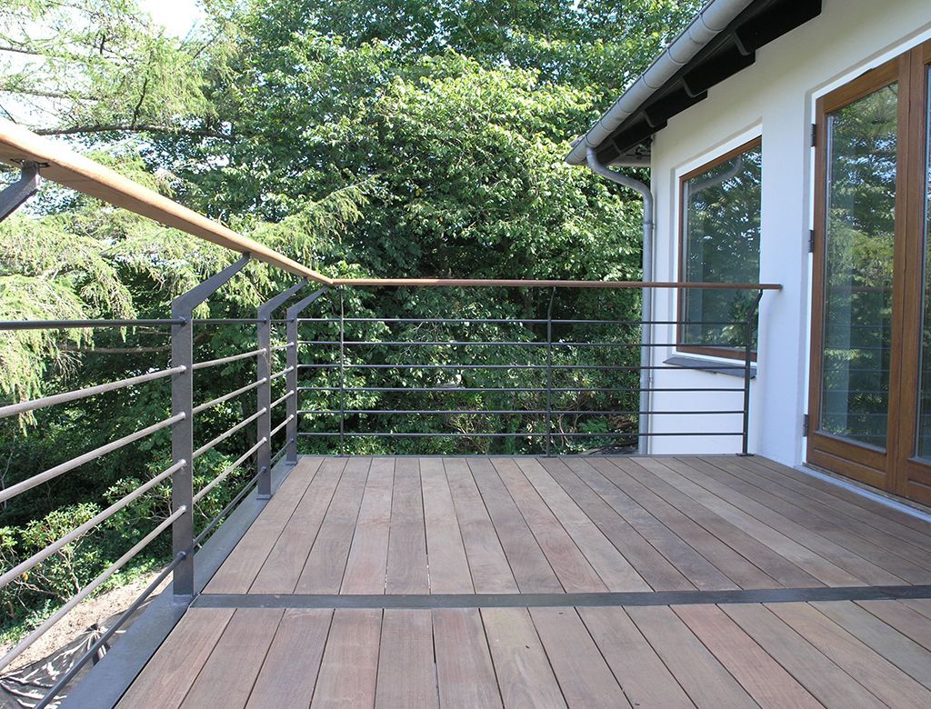 Træterrasse med metalrækværk og trægelænder med udsigt over træer.