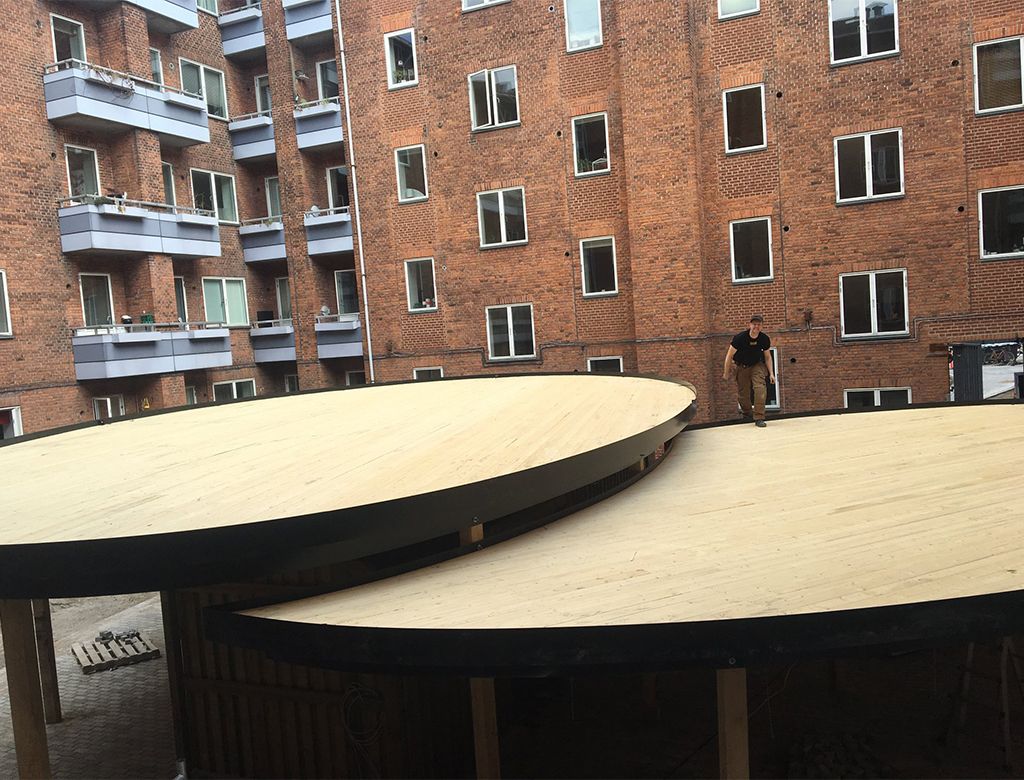 Person på et tag med en rødlig murstensbygning i baggrunden. To runde, lyse tage i forgrunden.