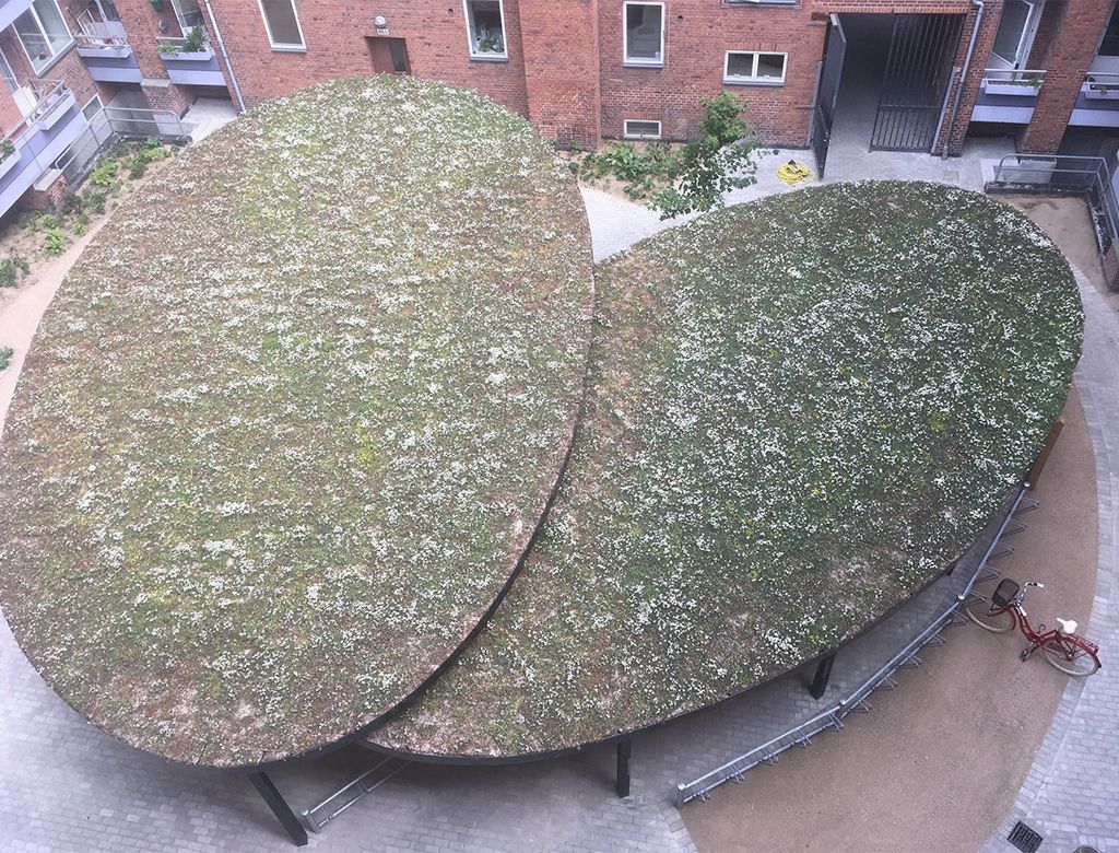 To store, ovale grønne tage i en bymæssig gårdsplads. Sorte metalstøtter og murstensbygninger omgiver det.