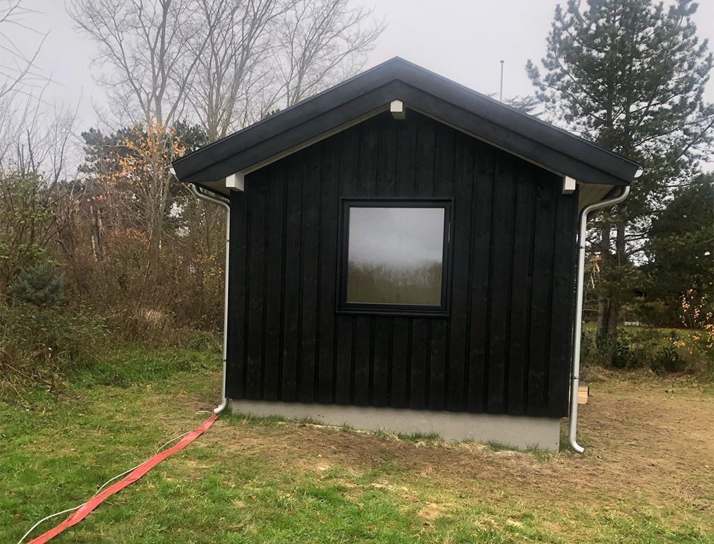 Sort træskur med et enkelt vindue på en græsklædt grund.