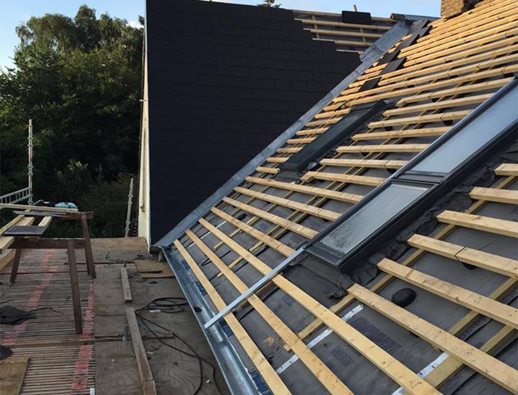 Tag delvist dækket med sorte teglsten, der viser synlige træskelet og ovenlysvinduer.