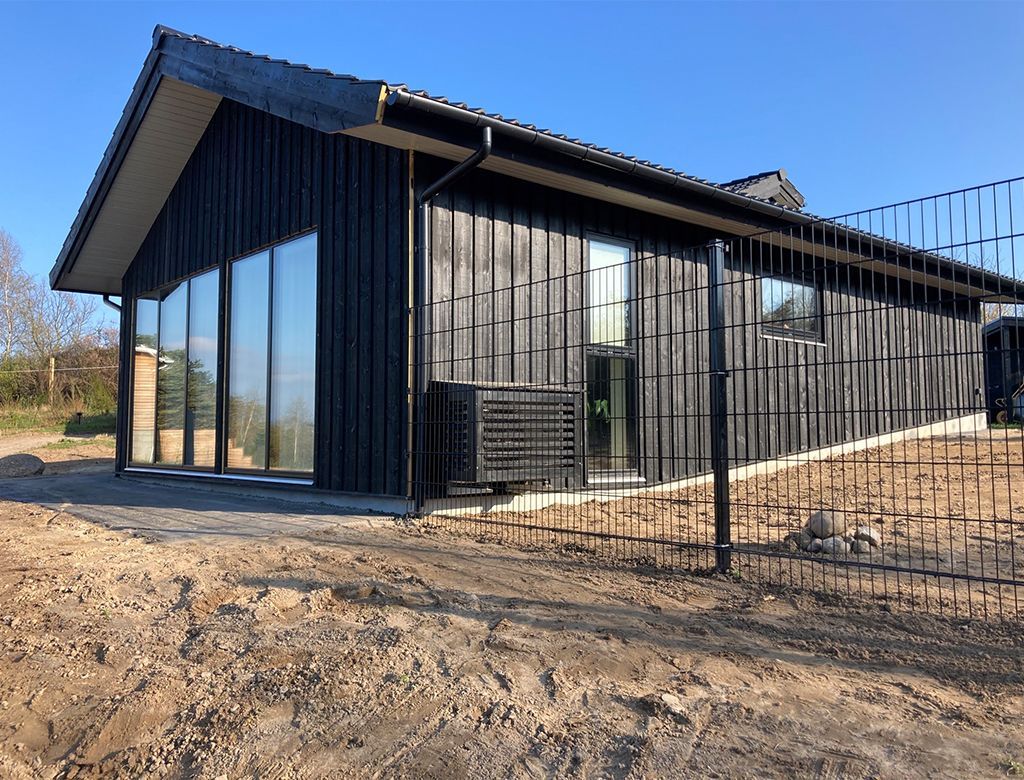 Sortklædt moderne bygning med store vinduer, beliggende på en byggeplads bag et sort metalhegn.