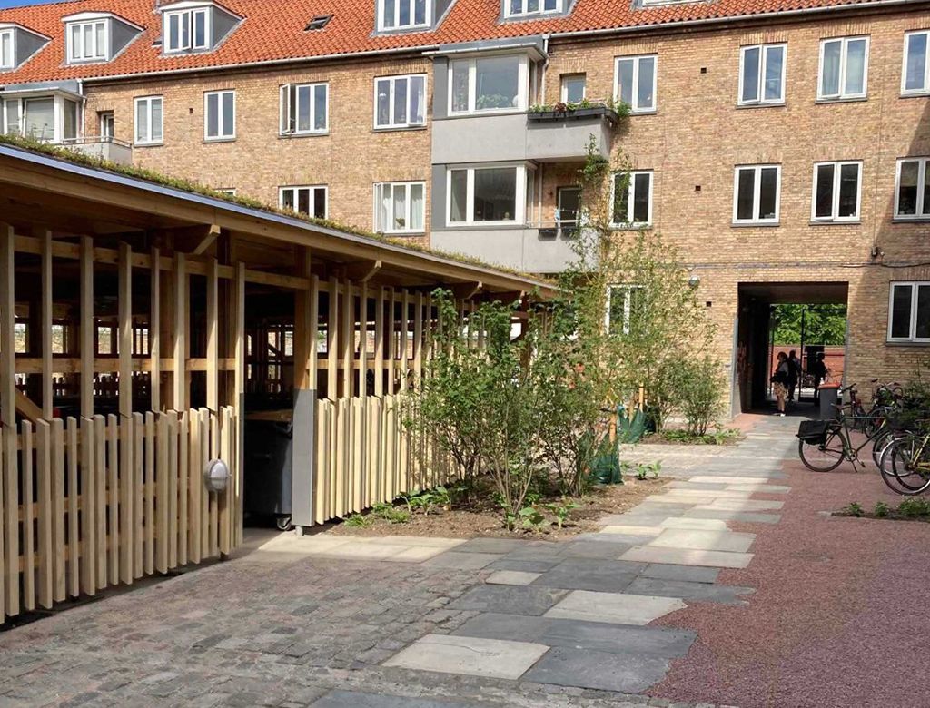 Gårdhave med murstensbygninger, cykelparkering og en lille have.