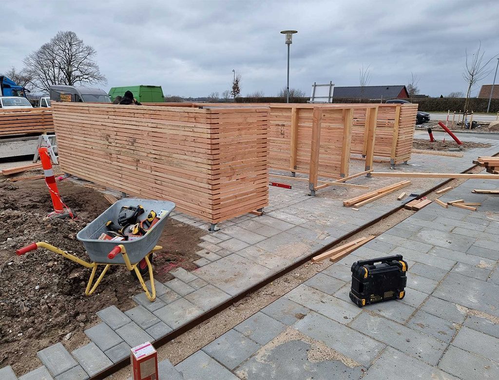 Byggeplads: delvist bygget træstruktur. Værktøj og materialer på jorden. Overskyet himmel.