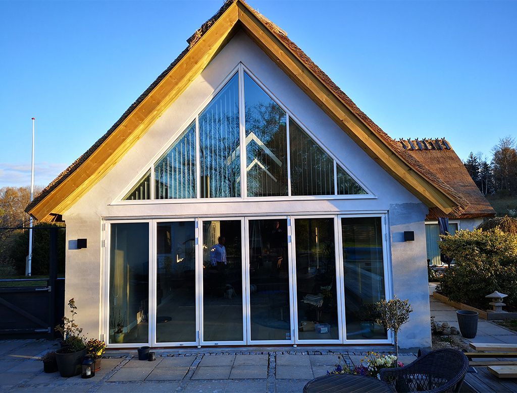 Hus med stråtag, trekantede glasvinduer og foldedøre i glas.