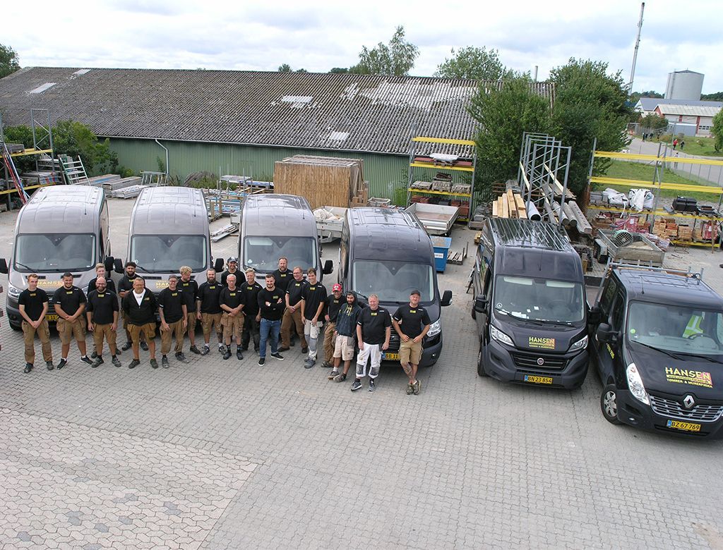 En gruppe bygningsarbejdere i uniform poserer foran varevogne på en arbejdsplads.