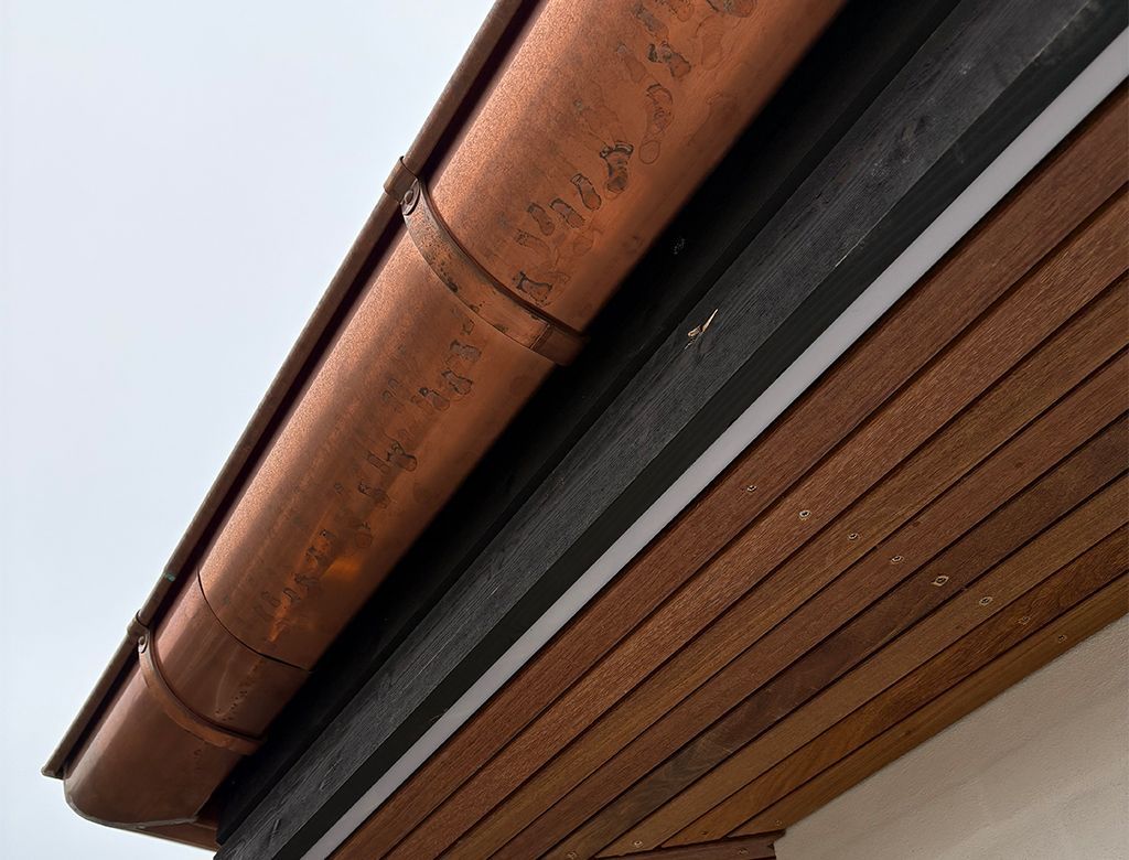 Kobberrende på en træbygning med brun facadebeklædning og en overskyet himmel.