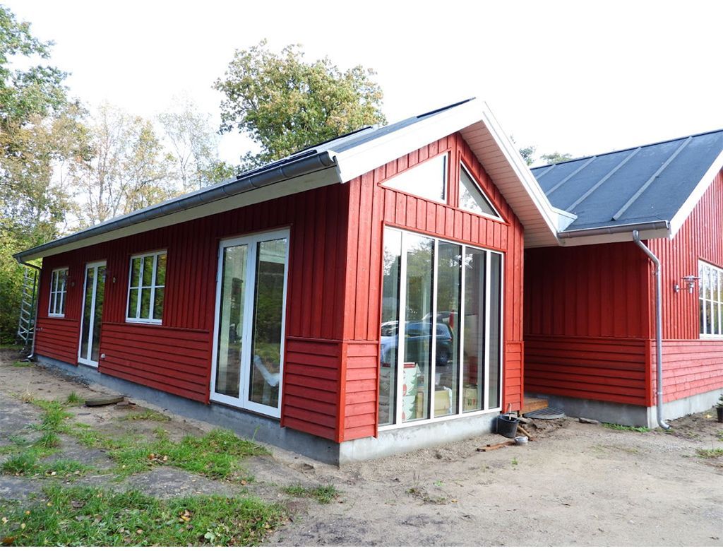 Rødt træhus med hvidindrammede glasdøre og -vinduer; gråt tag; udvendig udsigt.