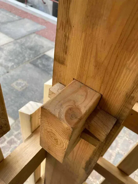 Samling af pergola i træ, med et rektangulært stykke fastgjort til en lodret bjælke.