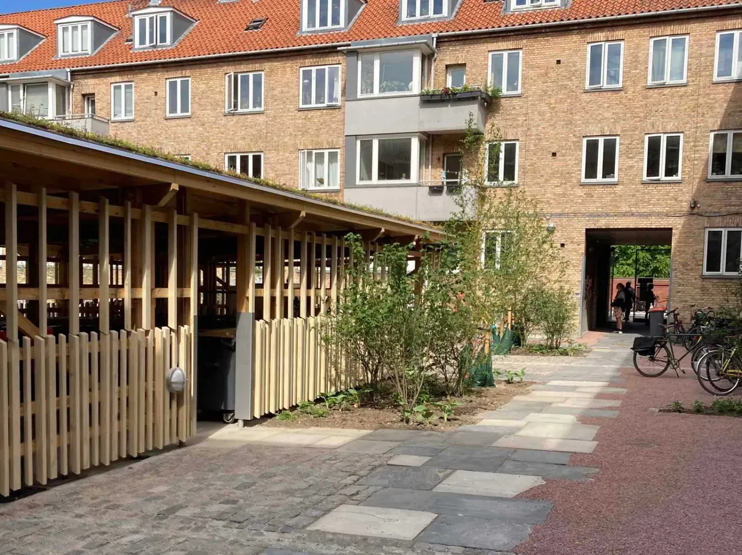 Gårdhave med træstrukturer, murstensbygninger og grønne områder.