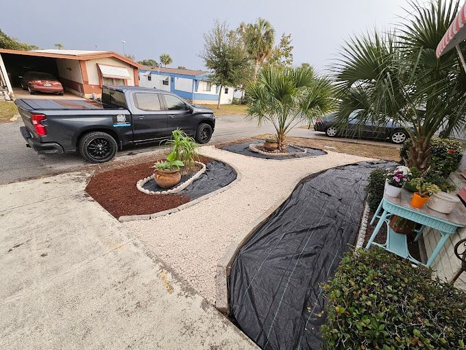 Landscaped yard with gravel, mulch, and plants in front of mobile homes; a black truck is parked nearby.