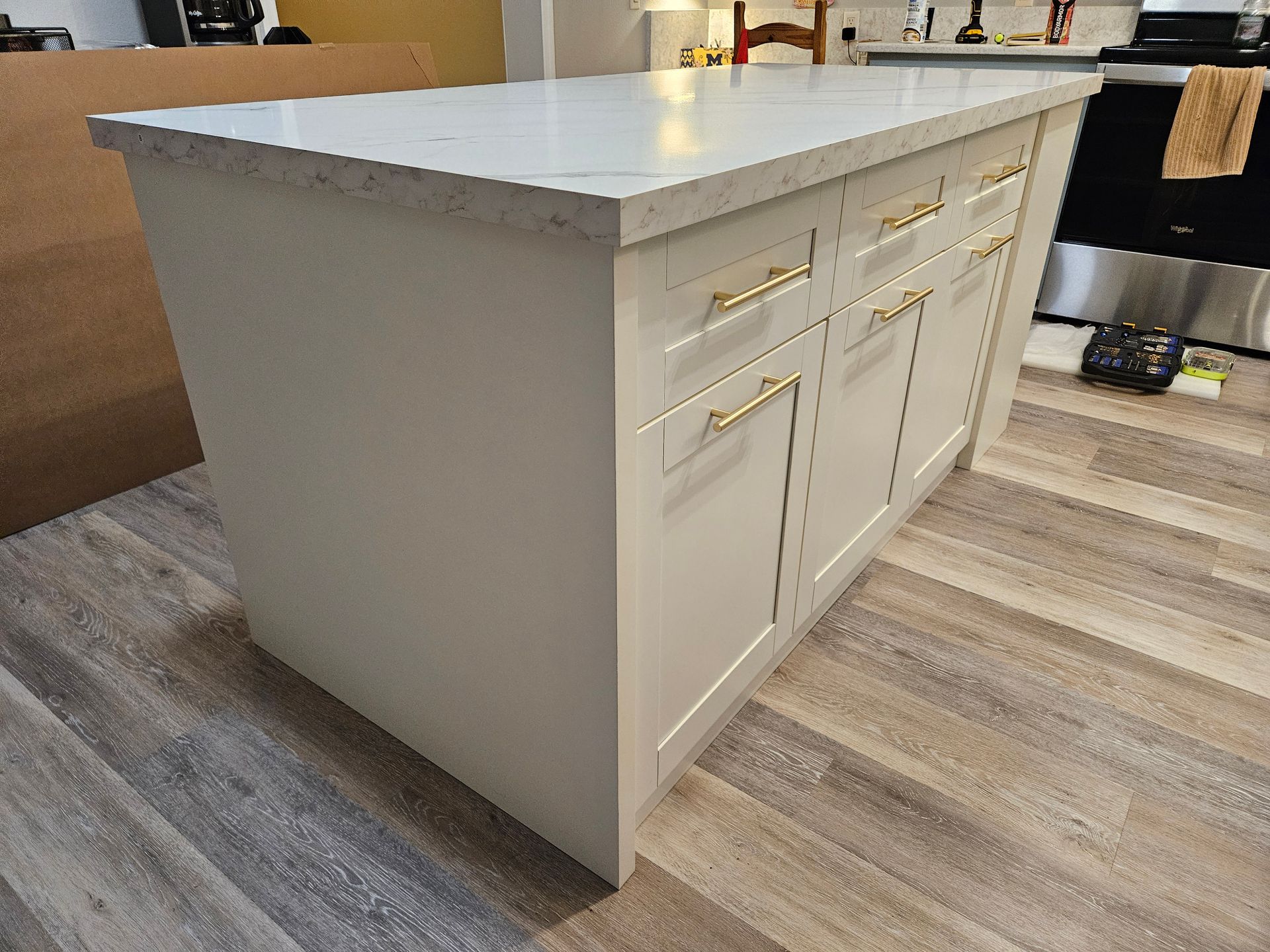 A kitchen island with a white countertop and cabinets, with gold handles on a wooden floor.