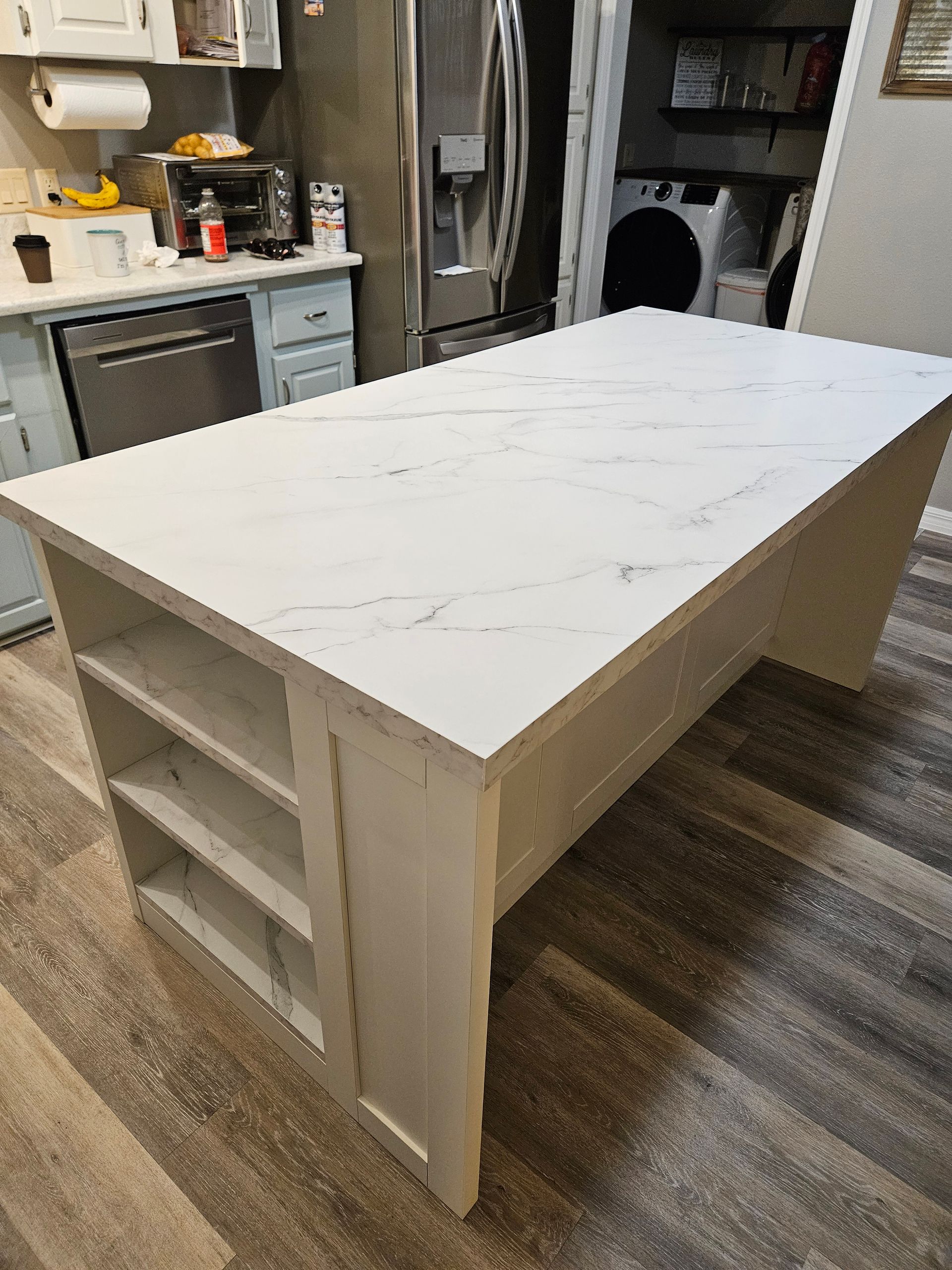 Kitchen island with white countertop and shelves, standing on a gray wooden floor.