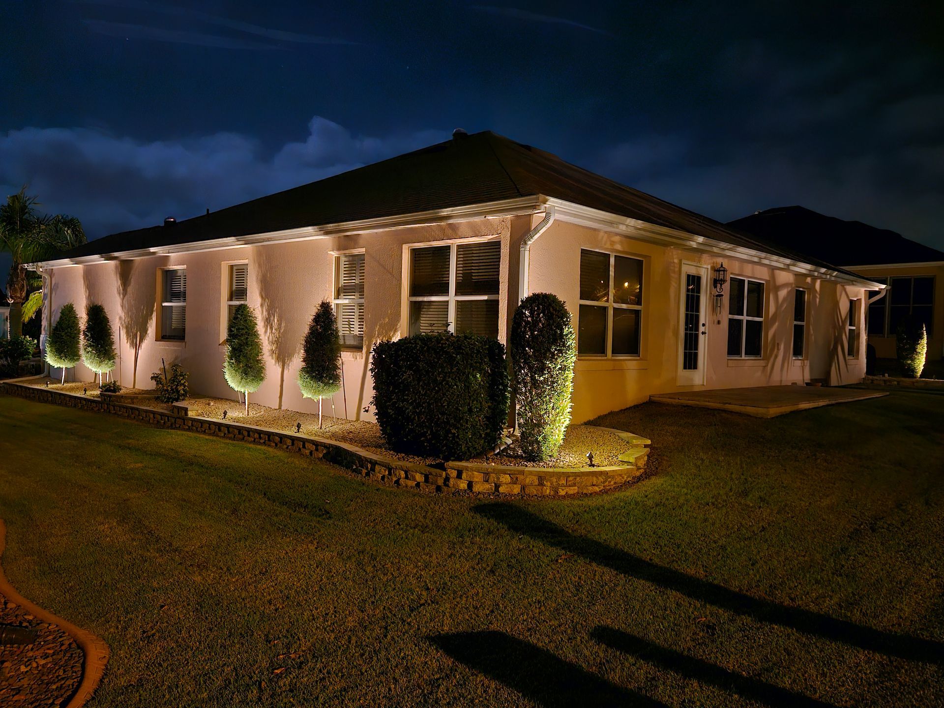 Night view of a house with exterior lights illuminating landscaping and facade against a dark sky.