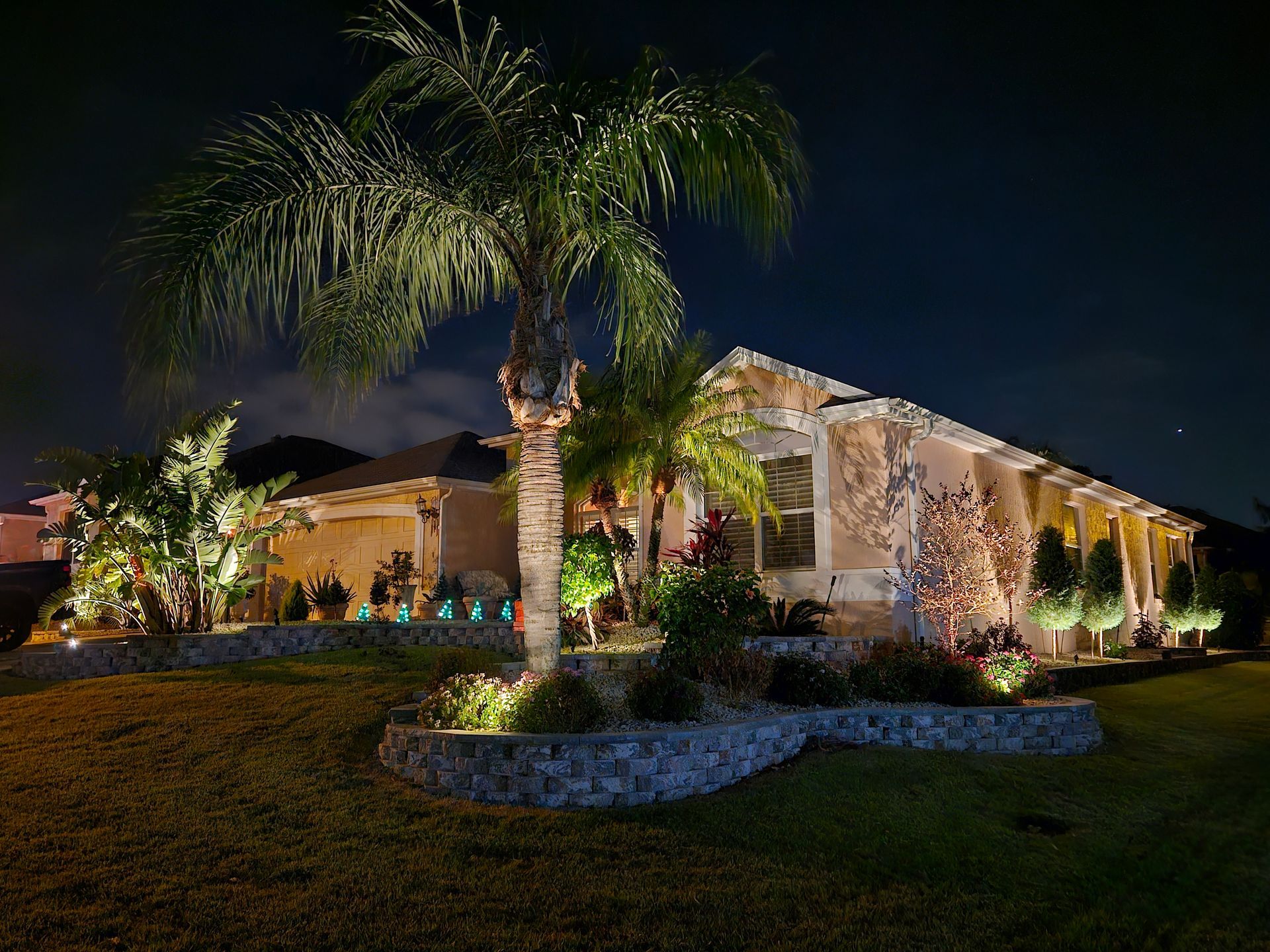 Nighttime view of a home with landscape lighting highlighting the architecture and palm trees, against a dark sky.
