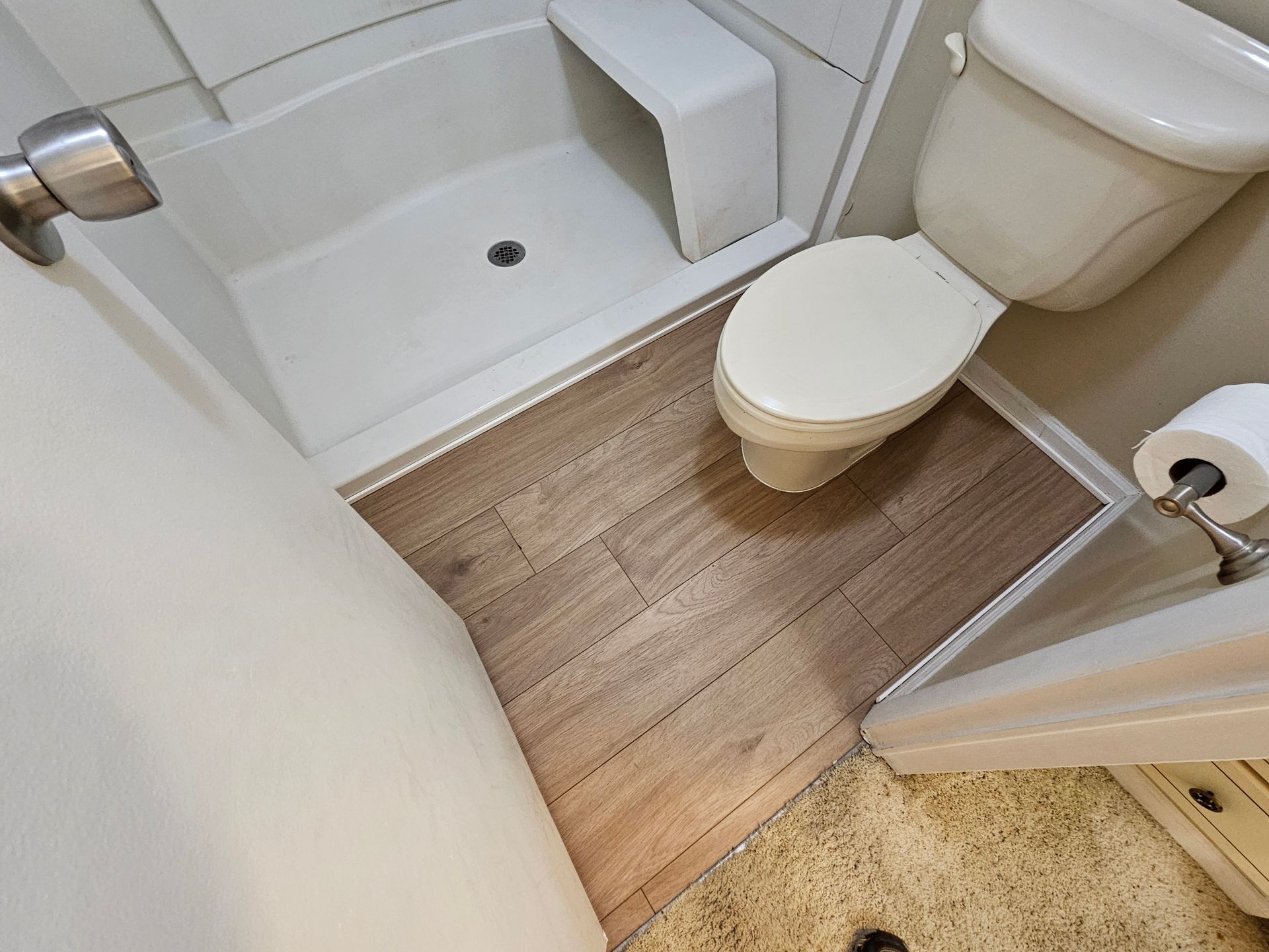 Bathroom with shower, toilet, and wood-look flooring. White walls and a neutral color palette.