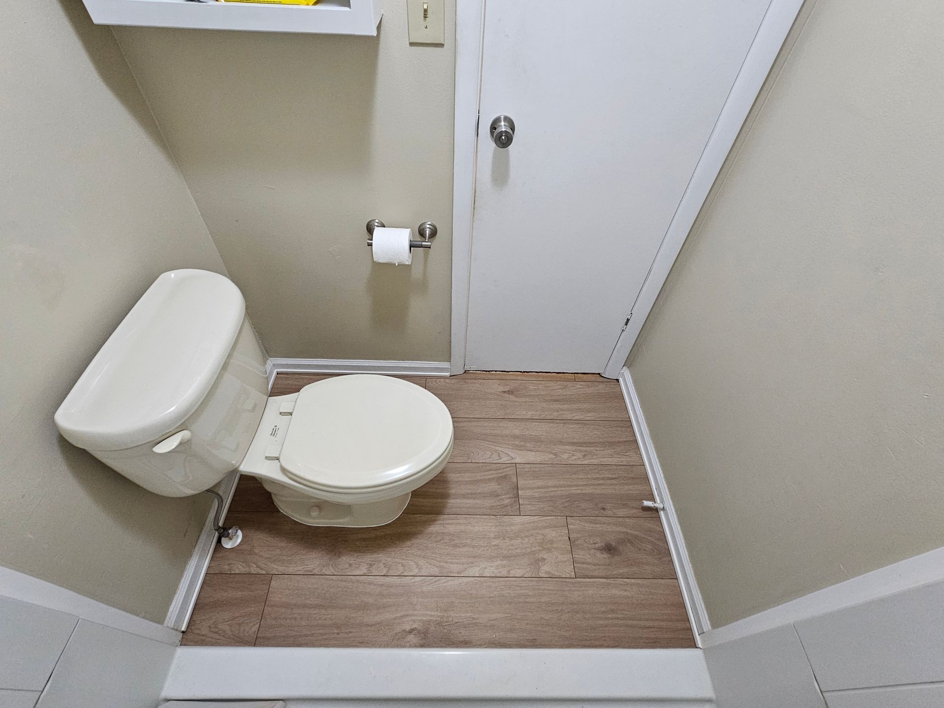 Small bathroom with toilet, wood-look floor, and white door.