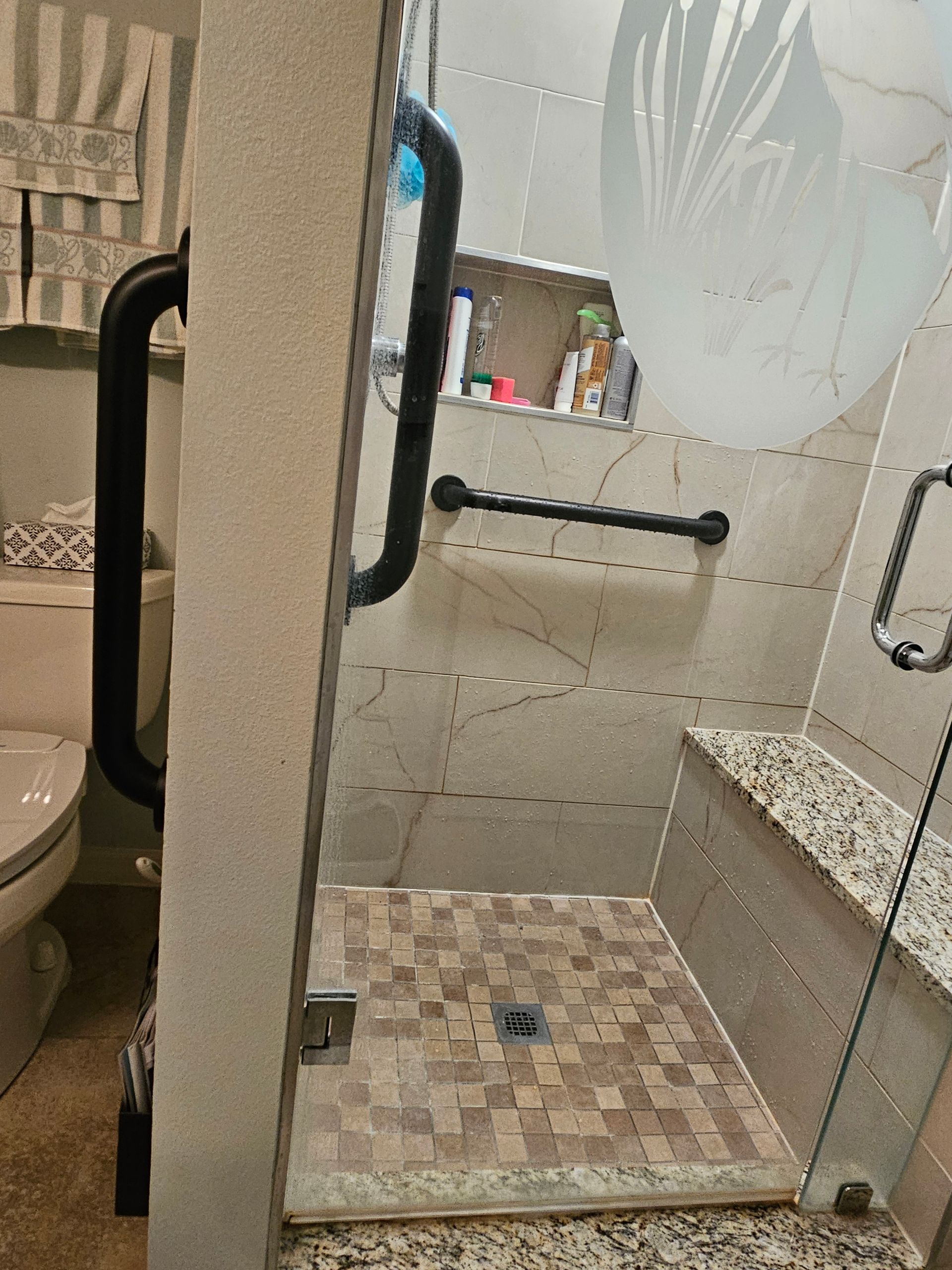 Accessible walk-in shower with grab bars, bench, and mosaic tile floor.