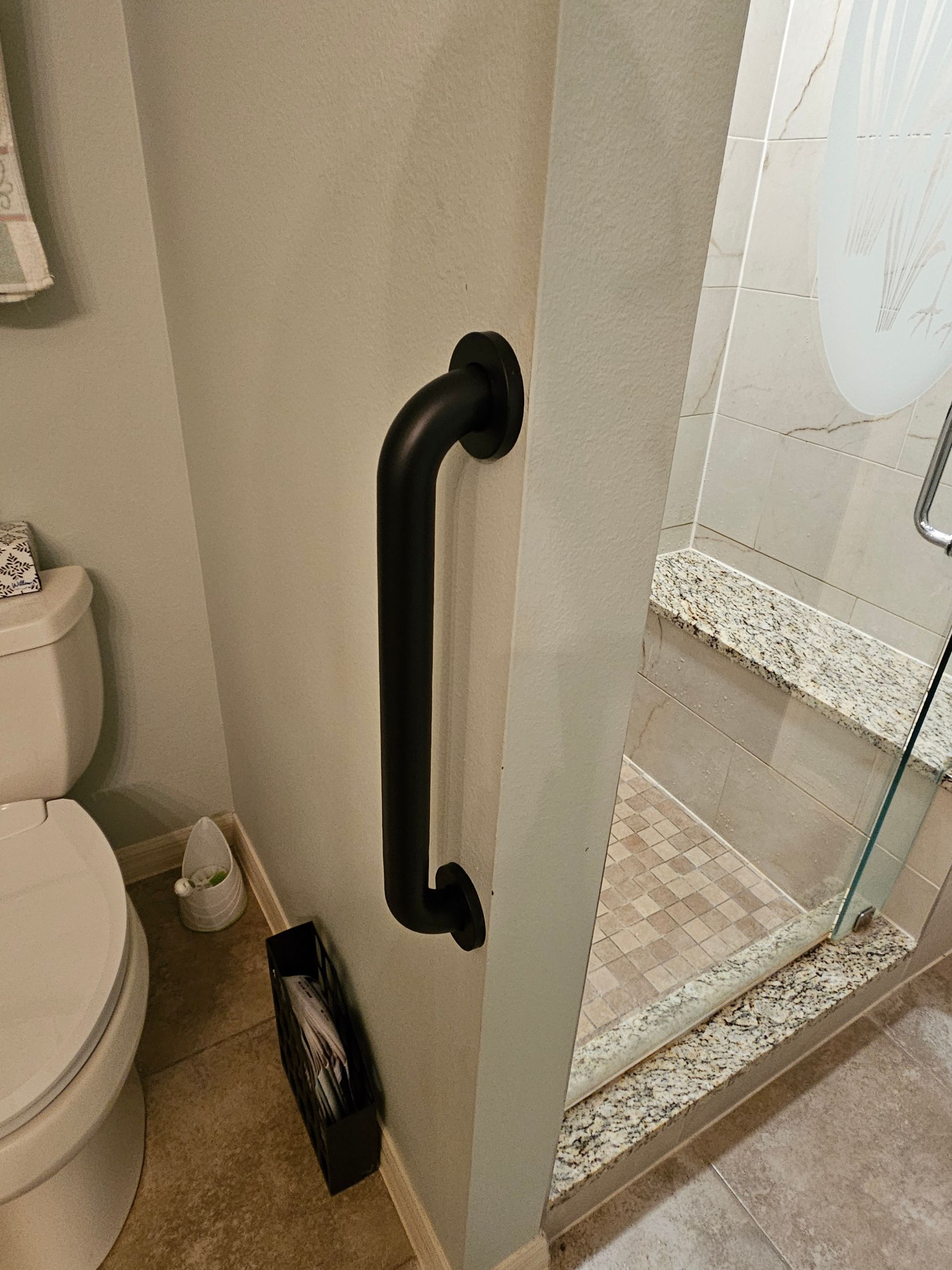 Black grab bar on a light-colored wall next to a glass shower door in a bathroom.