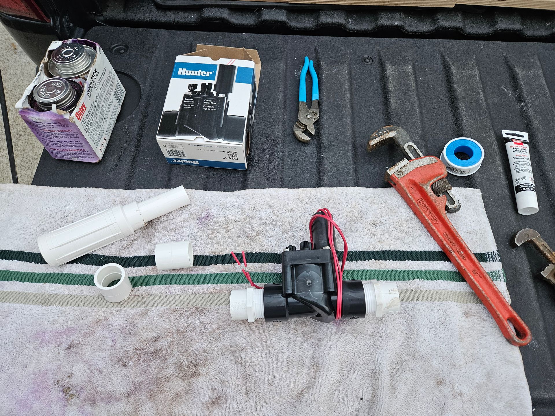 Irrigation valve, tools, and components arranged on a towel in a truck bed.