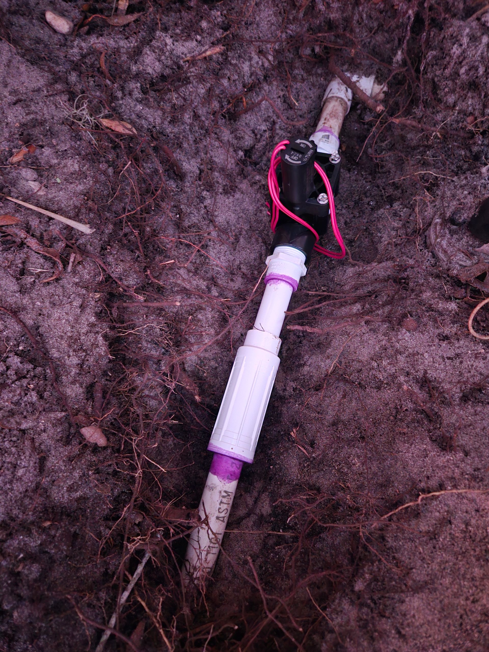 Irrigation valve buried in dirt with PVC pipes, wires and connector.